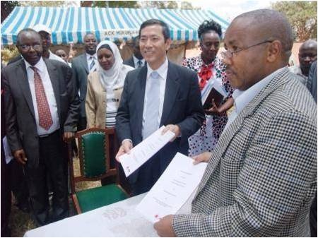 ムワンギ国会議員（左端）立会いの下、契約書を交わす高田大使（中央）とルノ氏（右）