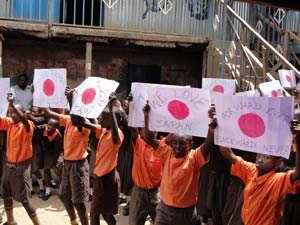 日本の復興を祈る歌を歌う生徒達：手には「日本・前進」「偉大な日本人」等激励のメッセージが書かれた紙製の国旗が。